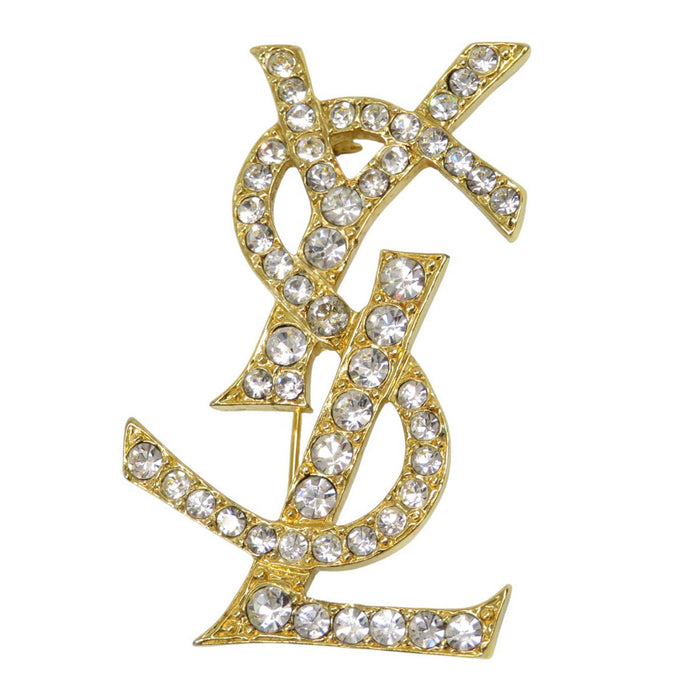 YVES SAINT LAURENT 
Metallo color oro 
Spilla con logo YSL e strass